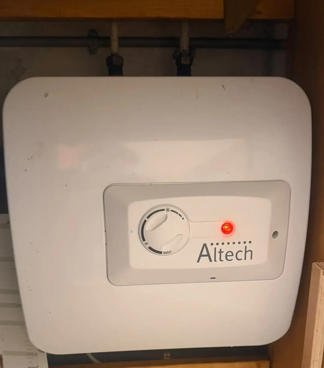 Petit chauffe-eau électrique blanc installé sous un évier de cuisine, voyant de chauffe allumé