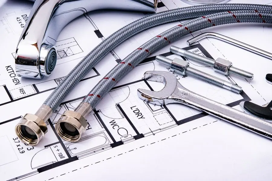 Clé, flexibles et robinet posés sur un plan de plomberie